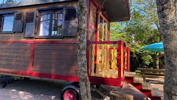 A wooden structure with a red and yellow railing, a window with shutters, and a small porch area. - Charmante Roulotte au Cœur de la Nature (Pigny)