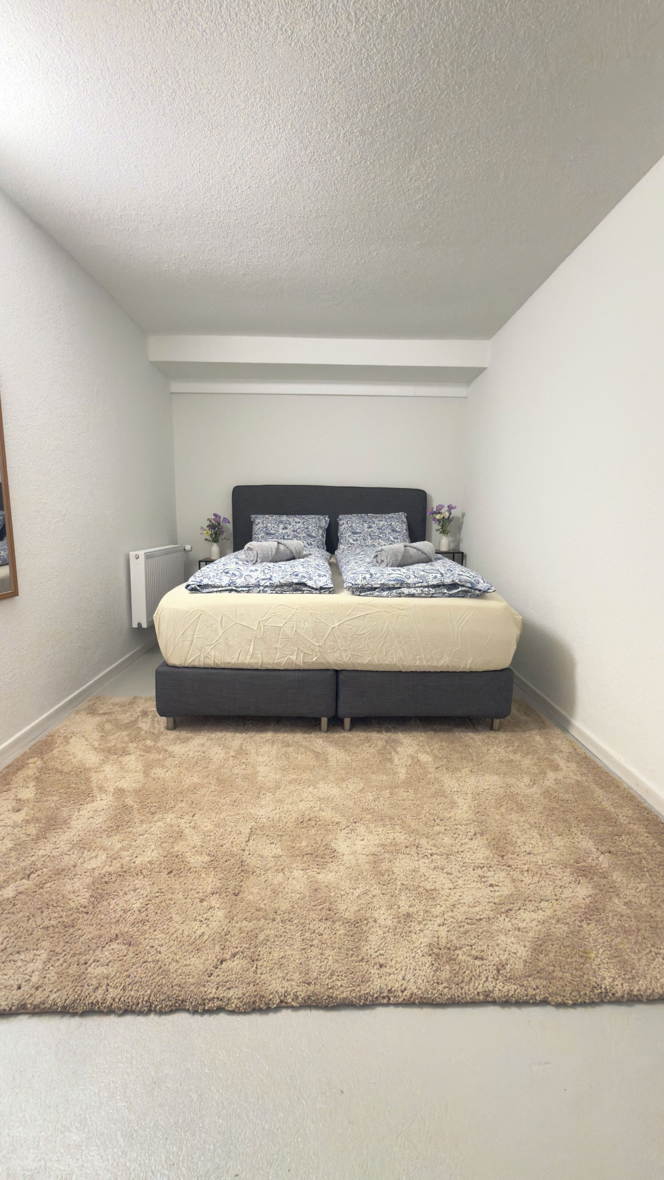 A bedroom with a bed, a radiator, and a carpet.
