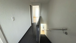 A hallway with a black tiled floor, a white wall with a light switch, and a door leading to another room.