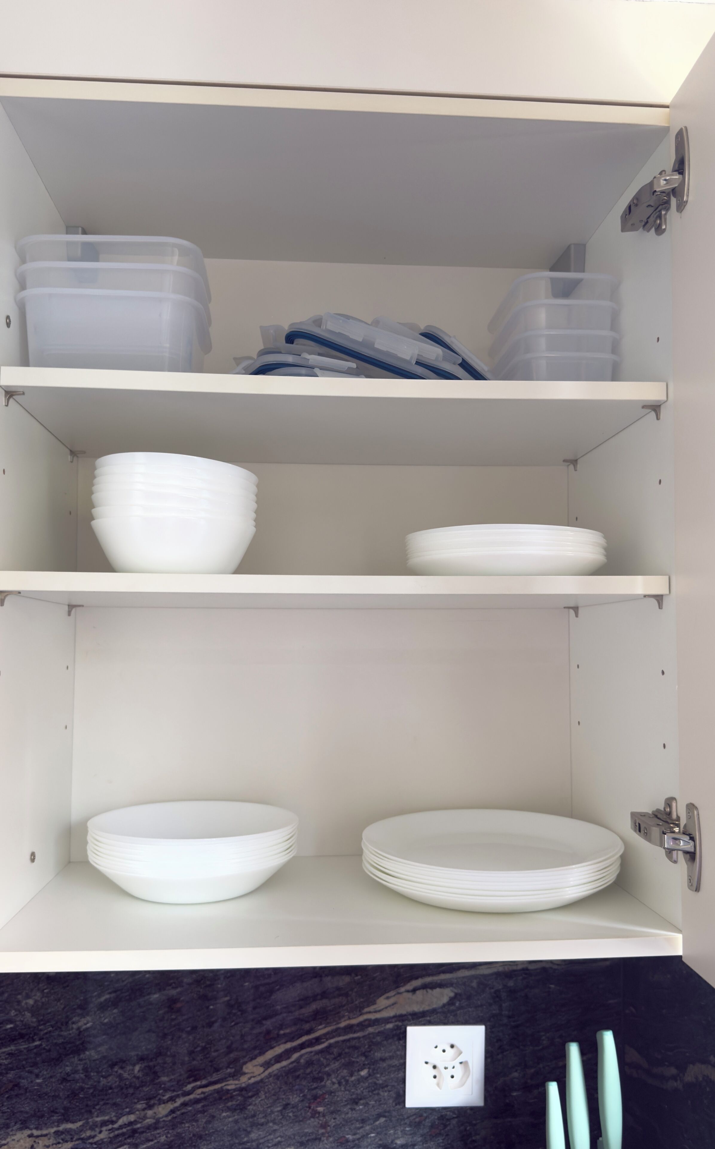 A kitchen cabinet with white storage shelves, a marble countertop, and a wall-mounted electrical outlet.