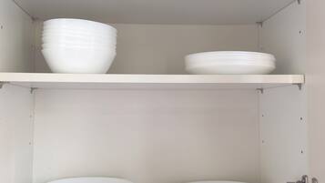 A kitchen cabinet with white storage shelves, a marble countertop, and a wall-mounted electrical outlet.