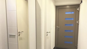 A hallway with a closed door at the end, a white wardrobe with a mirror, and a tiled floor.