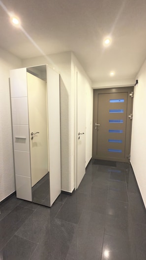 Ein Flur mit einer geschlossenen Tür am Ende, einem weißen Schrank mit Spiegel und einem gefliesten Boden.