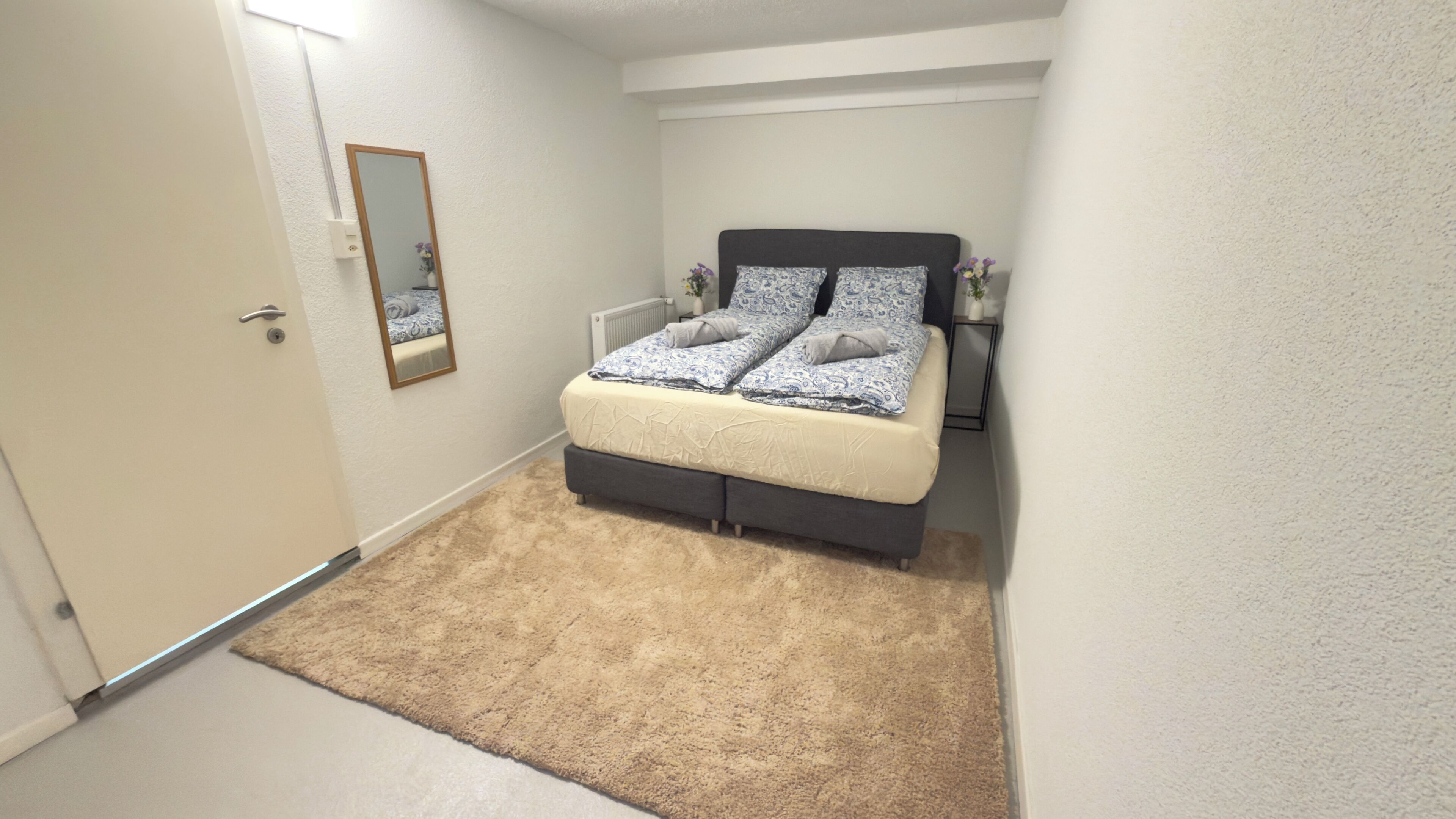 Un dormitorio con cama, mesita de noche, espejo y alfombra.