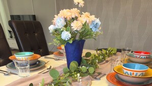 A dining table set with multiple bowls, plates, and cutlery, accompanied by a vase of flowers.