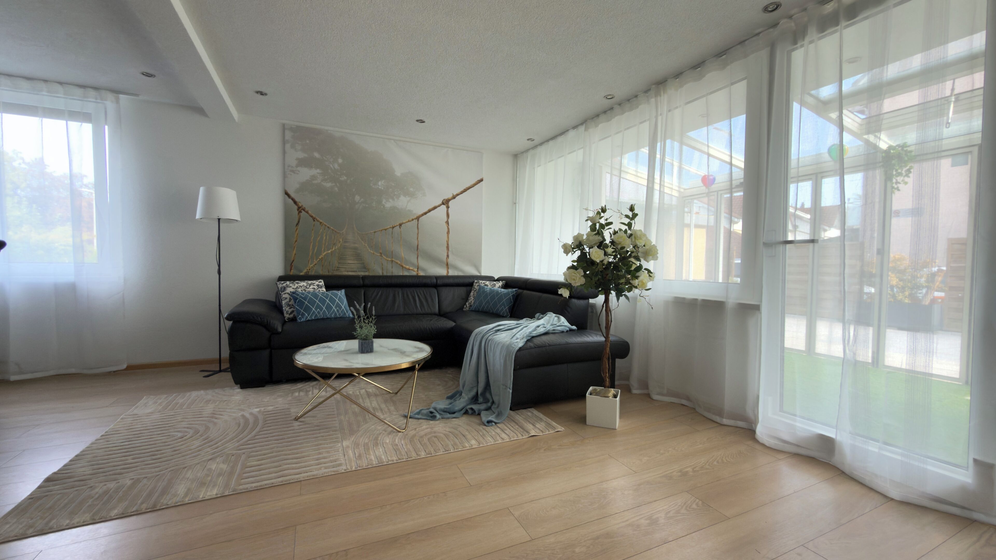 Ein modernes Wohnzimmer mit einem schwarzen Sofa, einem runden Couchtisch und einem großen Fenster mit transparenten Vorhängen.