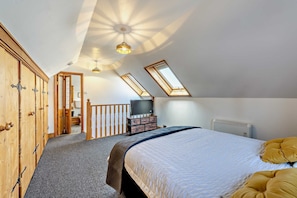 A bedroom with a sloped ceiling, skylights, a bed, a dresser, and a television. - Host & Stay | The Coach House (Worthing)
