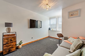 A modern living room with a flat-screen TV, a wooden sideboard, a grey sofa, and a small table. - Host & Stay | The Coach House (Worthing)