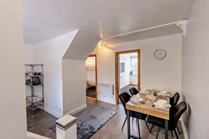 A dining area with a table set for four, a clock on the wall, and a kitchen visible through an open door. - Host & Stay | The Coach House (Worthing)
