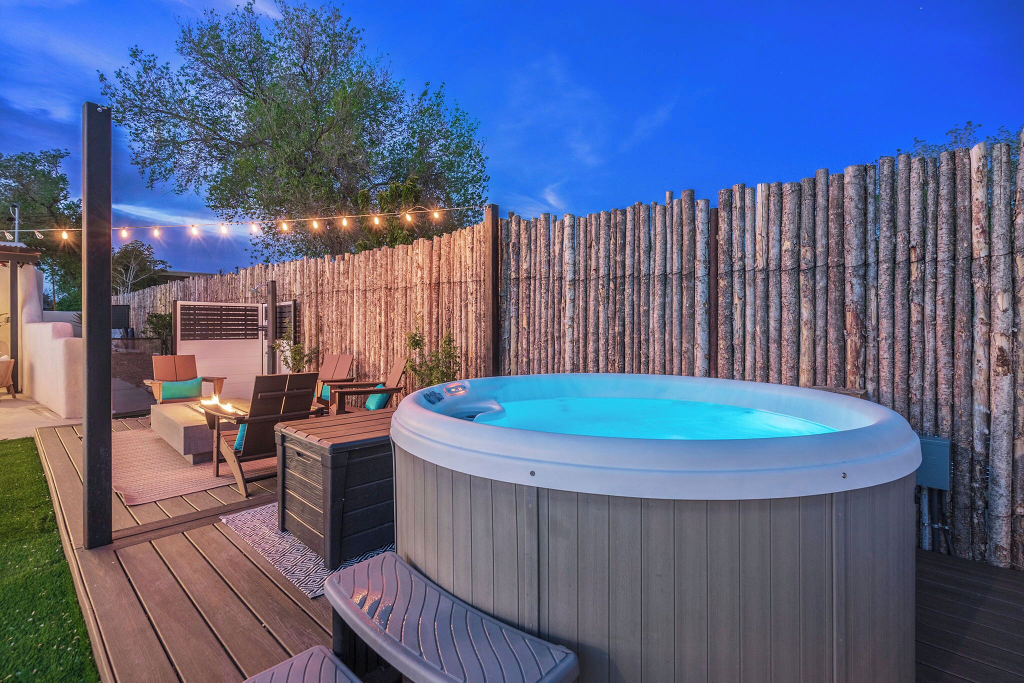 Ein Whirlpool auf einer Holzterrasse mit Gartenmöbeln und einem Bambuszaun.