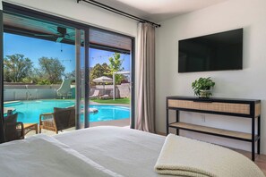 A bedroom with a large bed, a TV mounted on the wall, and a view of an outdoor swimming pool. - Resort-Style City Oasis with Heated Private Pool & Hot Tub (Santa Fe)