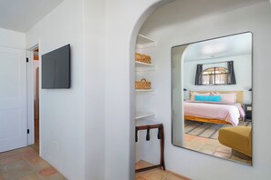 Ein Schlafzimmer mit einem Bett, einem Fenster mit Vorhängen, einem Nachttisch und einem Spiegel.