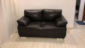 Un sofá de cuero negro en una habitación con piso de tonos claros y pared blanca.