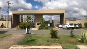 Un espacio de estacionamiento con un edificio al fondo, un banco en primer plano y un cielo despejado.