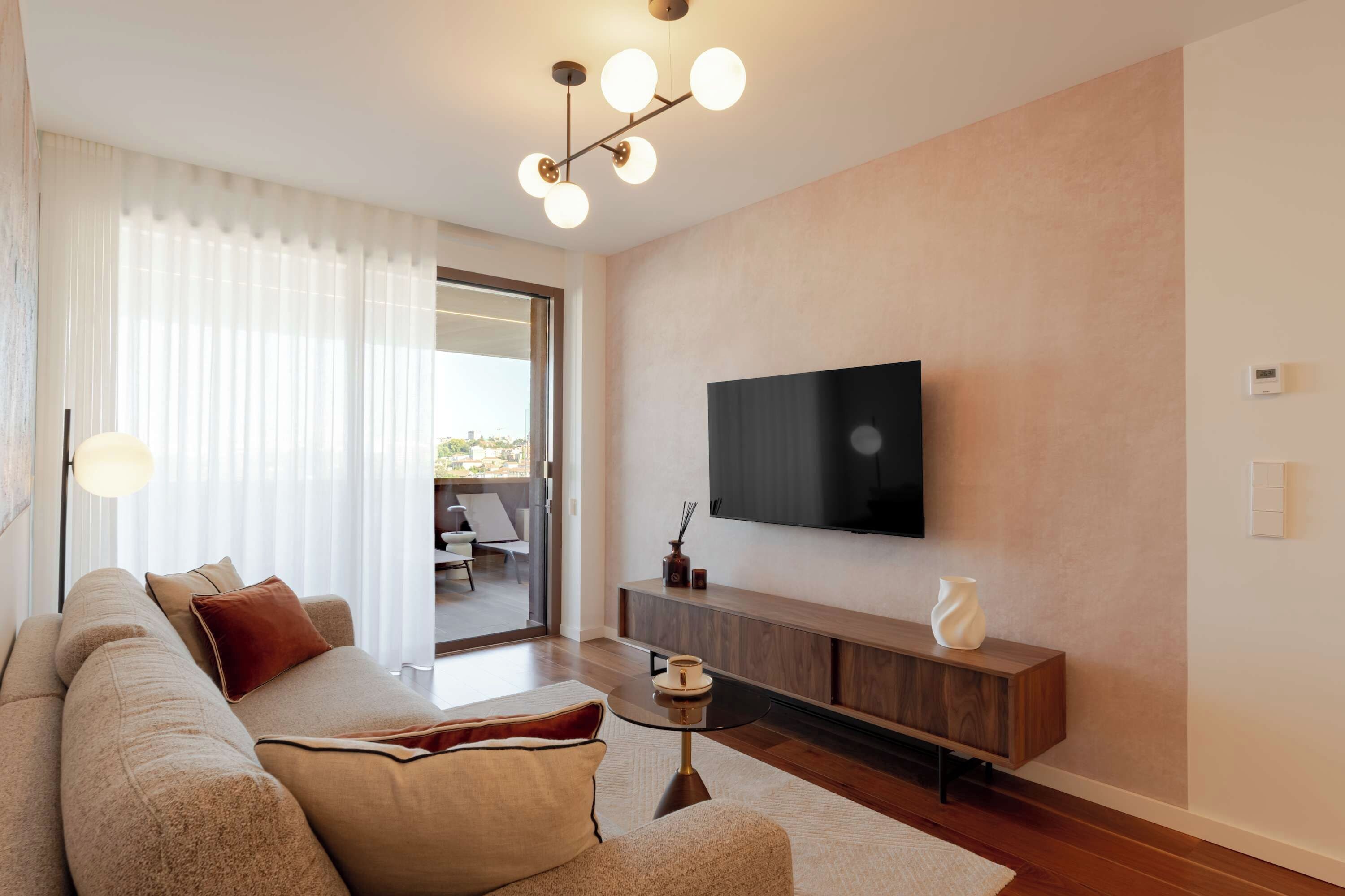 A modern living room with a sofa, TV, and a view through a glass door.