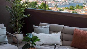 A balcony with a sofa, a table, a bottle, and glasses, overlooking a cityscape with a bridge. - Private Heated Pool & Dom Luis Views by HostWise (Vila Nova de Gaia)