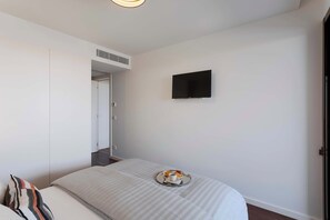 Ein Schlafzimmer mit einem Bett, einem flachbildfernseher an der Wand und einem Tablett mit Tasse und Gebäck auf dem Bett.