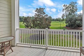 A porch with a view of a golf course, a wicker table, and a white railing. - World Tour Fairway Condo • Pool • 10 Min to Beach (Myrtle Beach)