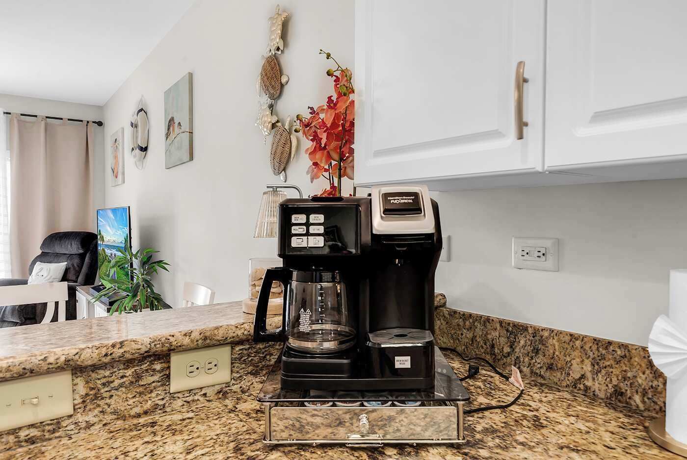 A kitchen with a coffee maker, a blender, and a glass carafe on a granite countertop.
