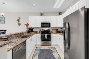 Eine moderne Küche mit weißen Schränken, Edelstahlgeräten, einer Granit Arbeitsplatte und einem gemusterten Teppich.