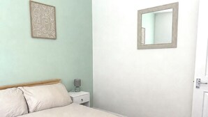 Quarto com cama, mesa de cabeceira, luminária, espelho e uma obra de arte na parede.