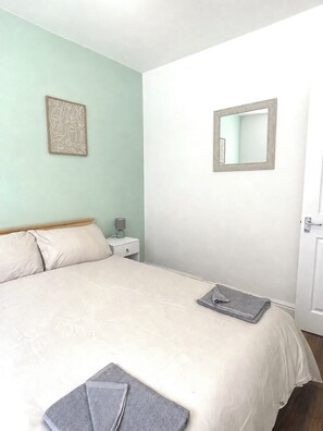Ein Schlafzimmer mit Bett, Nachttisch, Lampe, Spiegel und Wandbild.