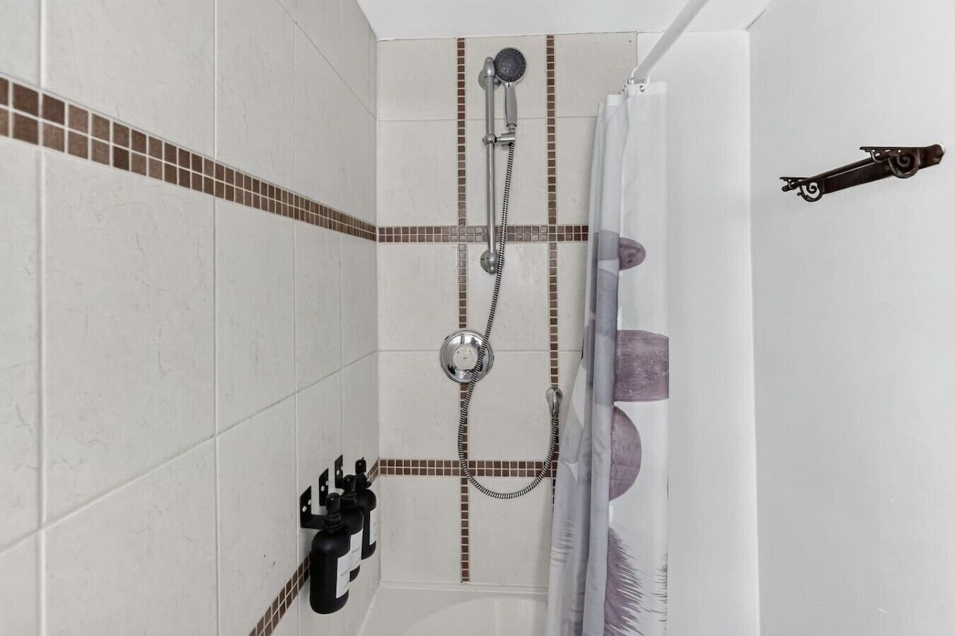 A shower with a handheld showerhead and a wall-mounted faucet, a shower curtain, and a towel rack with a towel.