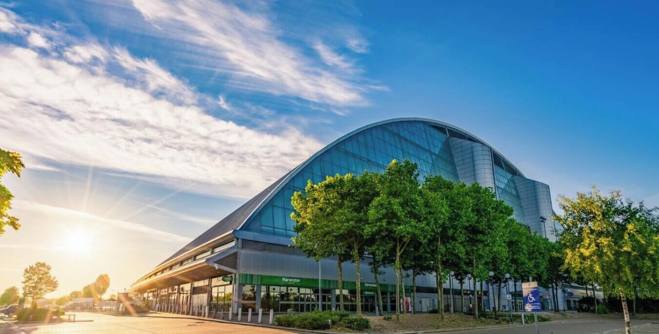 A modern building with a curved glass facade, surrounded by trees and a clear sky.