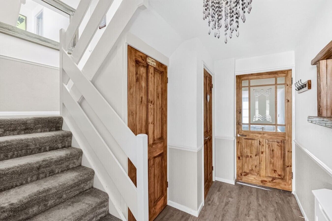 A staircase leading to a wooden door, a hallway with a wooden floor, and a chandelier.