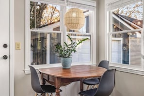 Un comedor con una mesa de madera, cuatro sillas, una planta en maceta y una lámpara colgante.