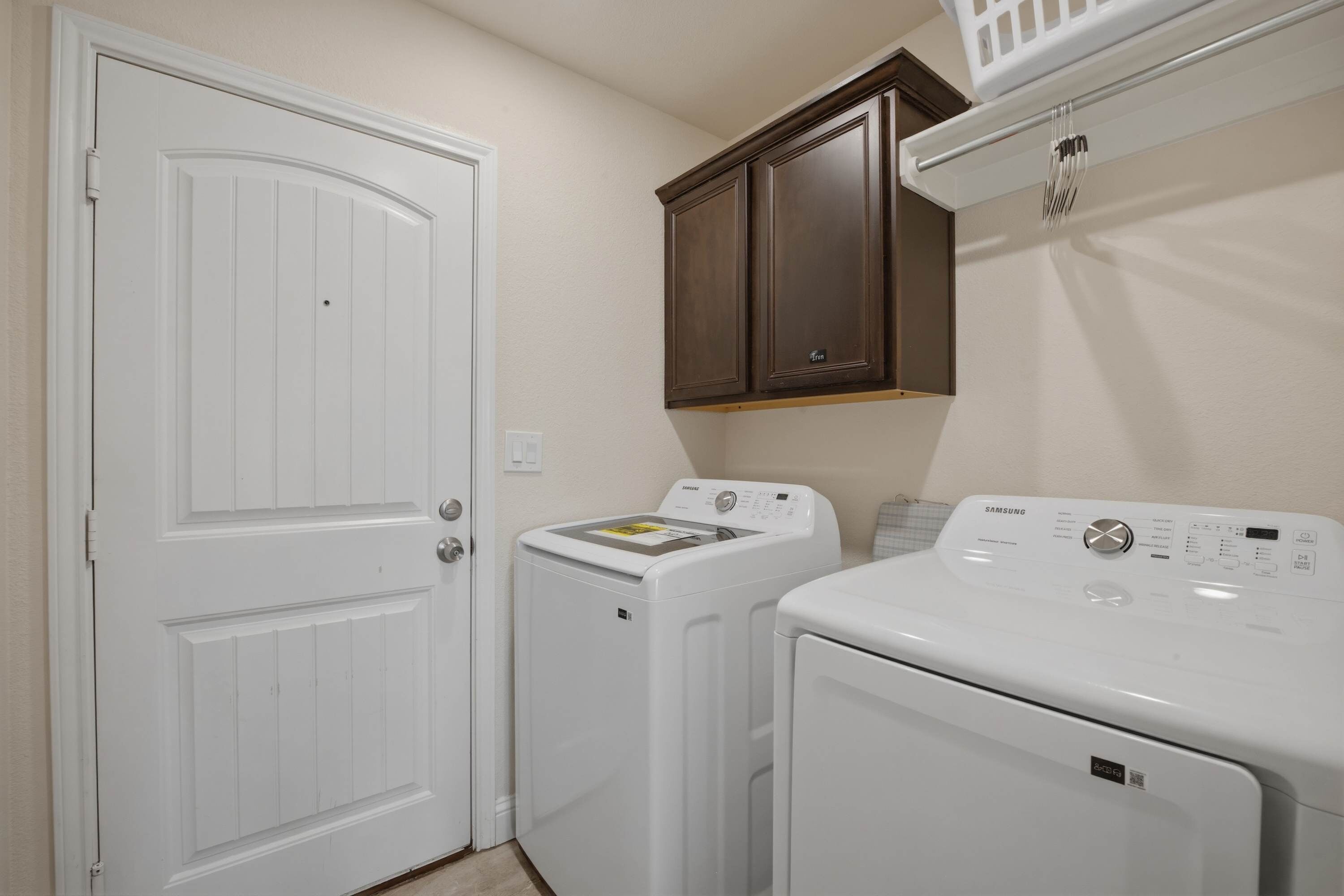 A laundry room with a white door, a washing machine, a dryer, and a cabinet above the dryer.