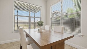 Un salón de conferencias con una larga mesa de madera, sillas blancas y grandes ventanales con persianas.
