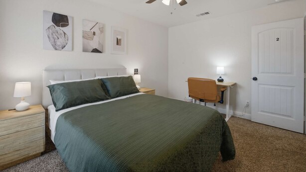 Un dormitorio con cama, escritorio, silla, ventilador de techo y una puerta.