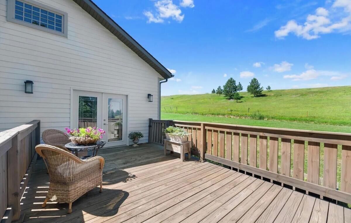 A wooden deck with wicker furniture and potted plants, overlooking a grassy landscape.