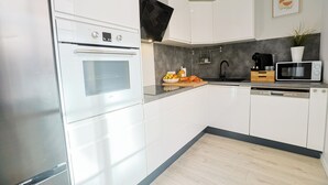 Una cucina moderna con mobili bianchi, forno a incasso, microonde e macchina per il caffè.
