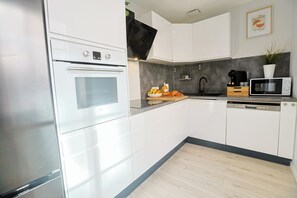 A modern kitchen with white cabinetry, a built-in oven, a microwave, and a coffee maker. - Le Petit Mont Blanc - Vue Église - Netflix - Wifi Fibre - Spacieux et Lumineux (Saint-Étienne)