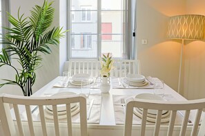 A dining table set with white plates, glasses, and cutlery, a vase with flowers, and a potted plant. - Le Petit Mont Blanc - Vue Église - Netflix - Wifi Fibre - Spacieux et Lumineux (Saint-Étienne)