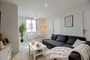 A modern living room with a grey sofa, white coffee table, and a dining area with a white table and chairs. - Le Petit Mont Blanc - Vue Église - Netflix - Wifi Fibre - Spacieux et Lumineux (Saint-Étienne)