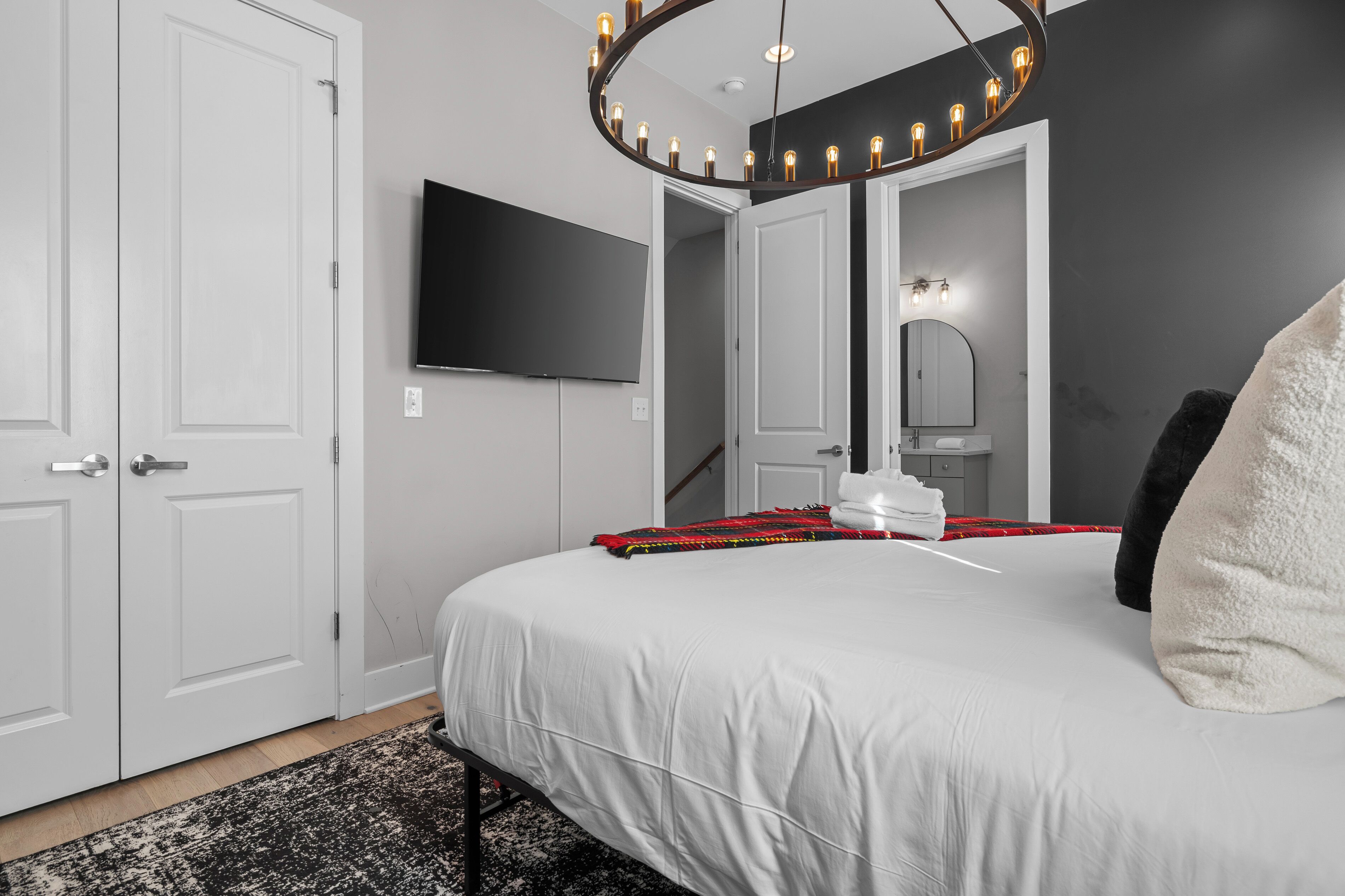 A bedroom with a bed, a television, a mirror, and a unique circular light fixture.