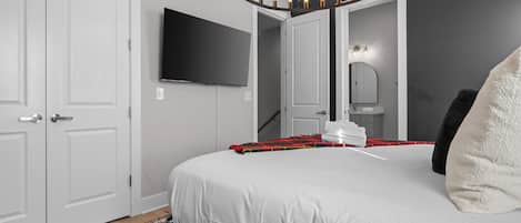 Une chambre à coucher comprenant un lit, un téléviseur, un miroir et un luminaire circulaire original.