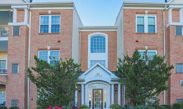 A multi-story brick building with a central entrance, numbered 10, and a clear sky above.