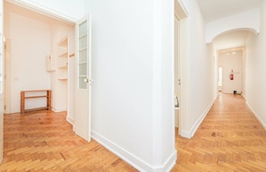 Ein Flur mit Holzboden, weißen Wänden und einer Tür zu einem Zimmer mit Fenster und Ablagefläche.