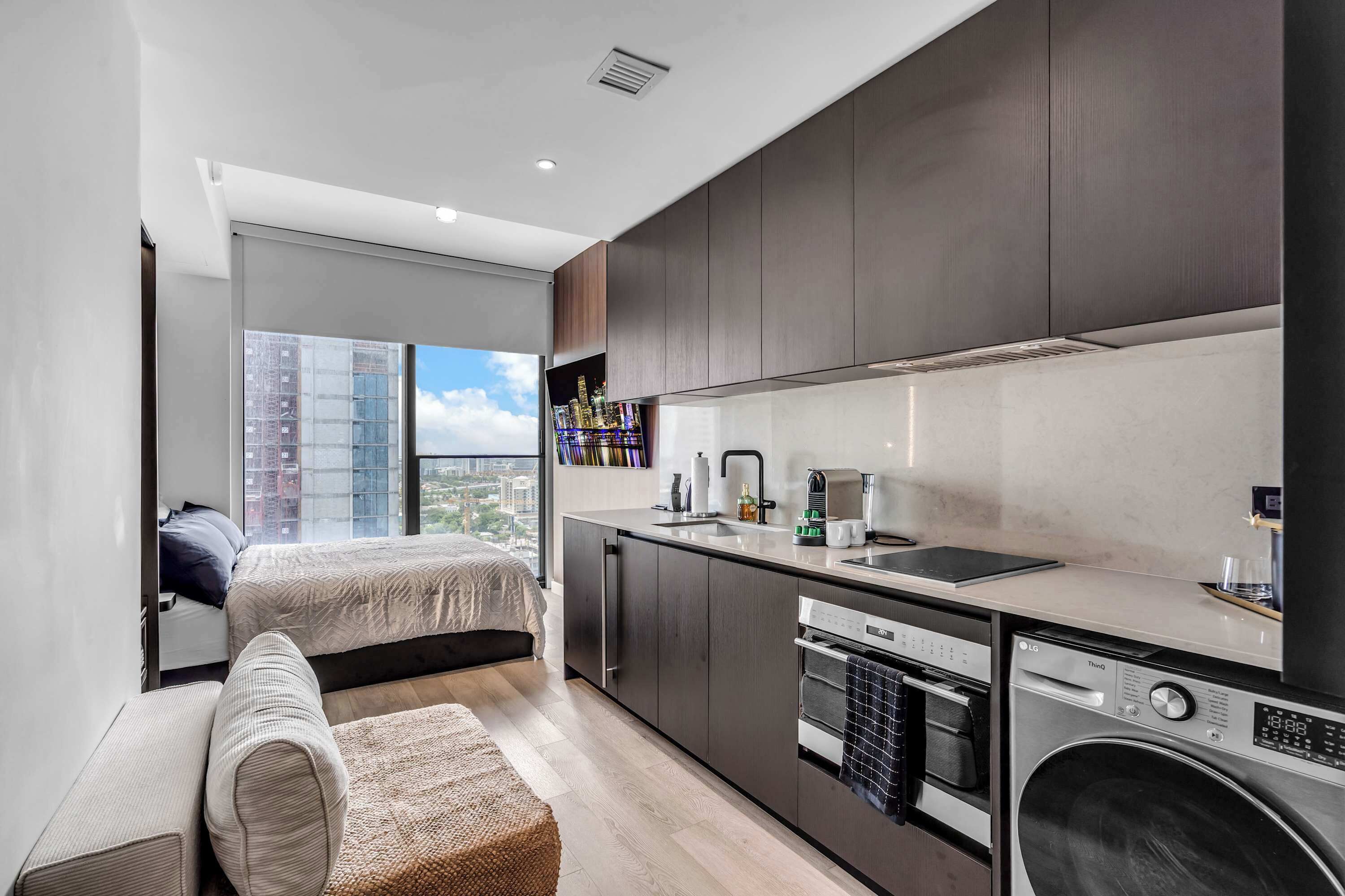 A modern apartment with a kitchenette, a bed, and a view of a cityscape.