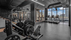 A gym with weightlifting equipment, treadmills, and large windows offering a city view. - Pied A Terre With Roof Pool (Miami)