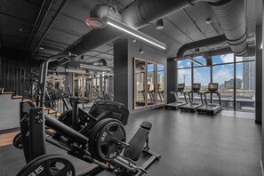 Ein Fitnessstudio mit Gewichthebern, Laufbändern und großen Fenstern mit Blick auf die Stadt.
