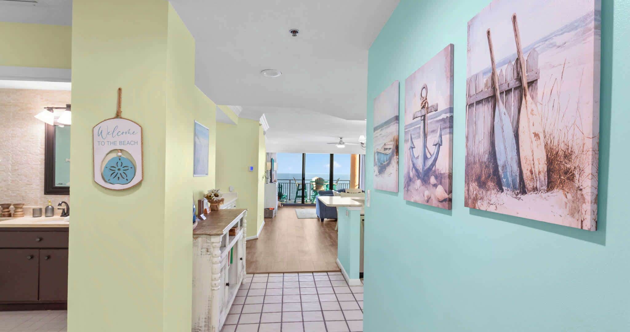 A hallway with a kitchen area, a dining space, and artwork on the walls.