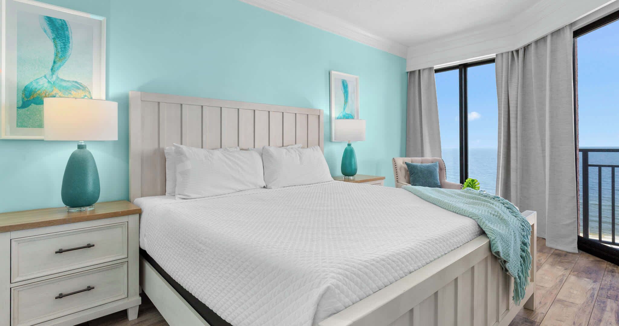 A hotel room with a bed, nightstands, a chair, a window with a view, and artwork on the walls.