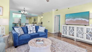 A living room with a blue sofa, a round coffee table, and a white cabinet with glass doors. - Seaside Sanctuary - Beachfront (Orange Beach)