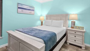 A bedroom with a bed, nightstands, a lamp, and a painting on the wall. - Seaside Sanctuary - Beachfront (Orange Beach)