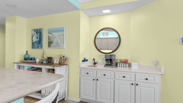 A kitchen with a marble countertop, white cabinets, a coffee machine, and two framed artworks on the wall. - Seaside Sanctuary - Beachfront (Orange Beach)